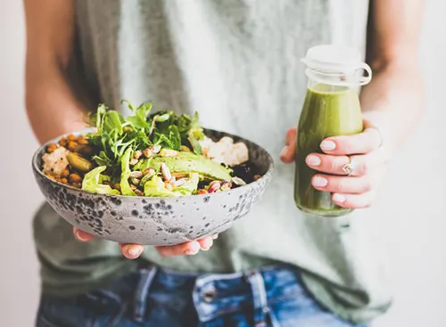 A person holds a salad of greens, nuts and grains with a bottle of creamy green dressing.