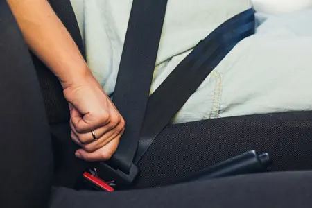 A pregnant person buckles a seatbelt.