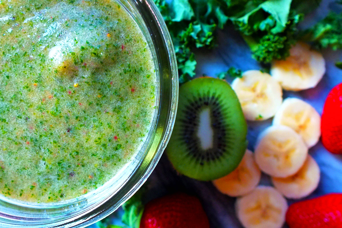 A green smoothie with sliced fruit in the background.