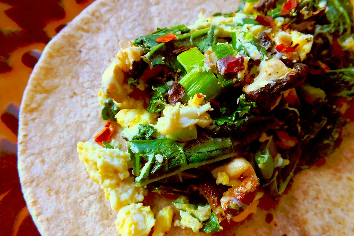 Eggs and vegetables are piled in a tortilla ready for rolling.