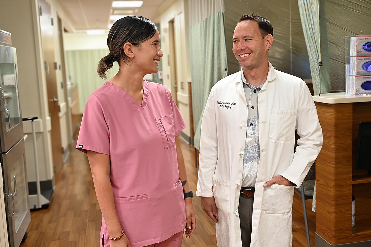 Two medical professionals standing in a clinic hallway one in pink scubs one in a white coat.
