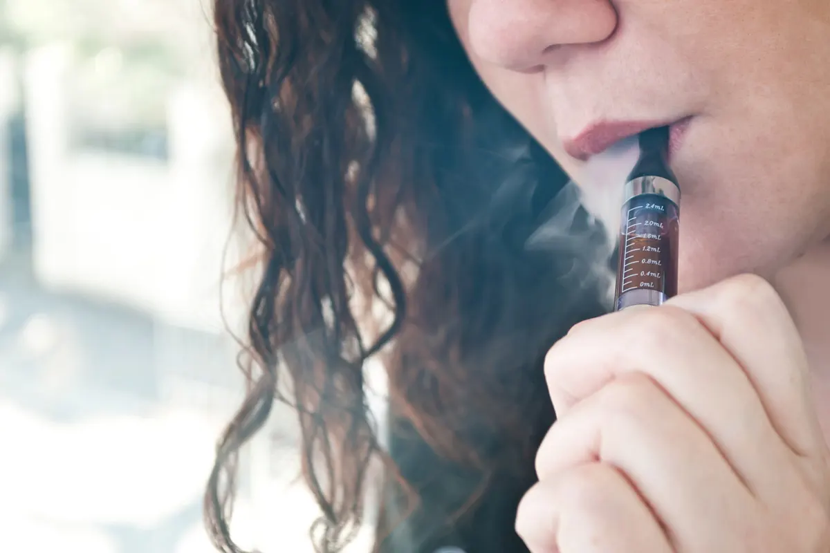 Closeup of young woman taking a hit from an electronic smoking device with smoke swirling around her head.