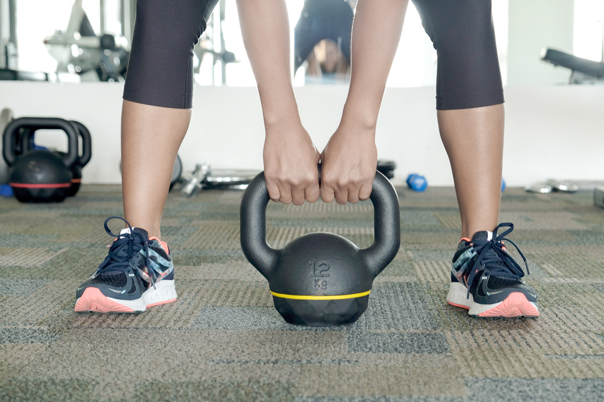 A woman in athletic clothes bending over to pick up a kettlebell.