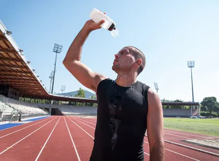 A man pours water over his head on a running track.