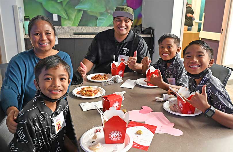 Family with three boys smiling, throwing shaka and having a meal at a table with handmade heart decorations.