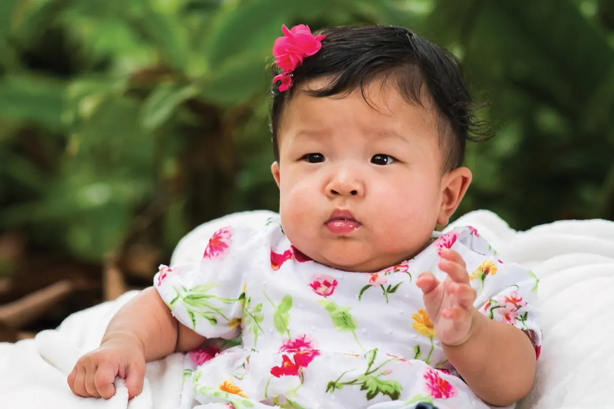One-year-old Kalley-Mae wearing a flower dress with a pink flower clip in her hair.
