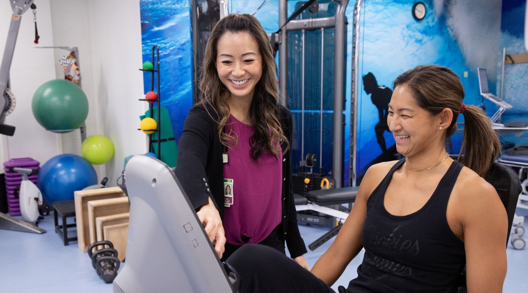 Physical therapist guides a patient using exercise equipment in a rehabilitation gym.