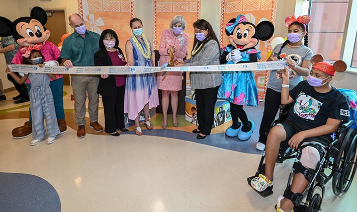 Kapiolani team members, patients, and Disney characters at a ribbon cutting.