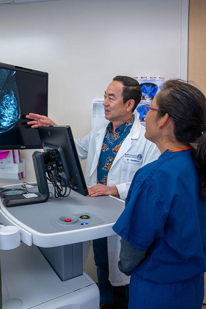 Doctor in white coat standing and gesturing to a monitor while speaking with a colleague in scrubs.