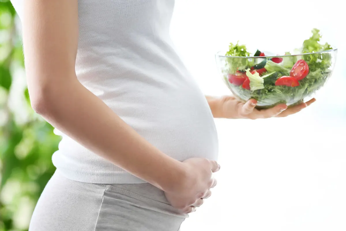 A pregnant Woman holding a healthy salad.