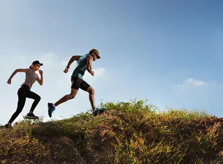 Two people trail running under a sunny blue sky.