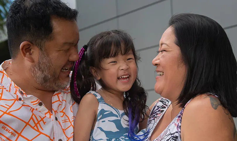 Kalley-Mae laughing in her parents' arms.