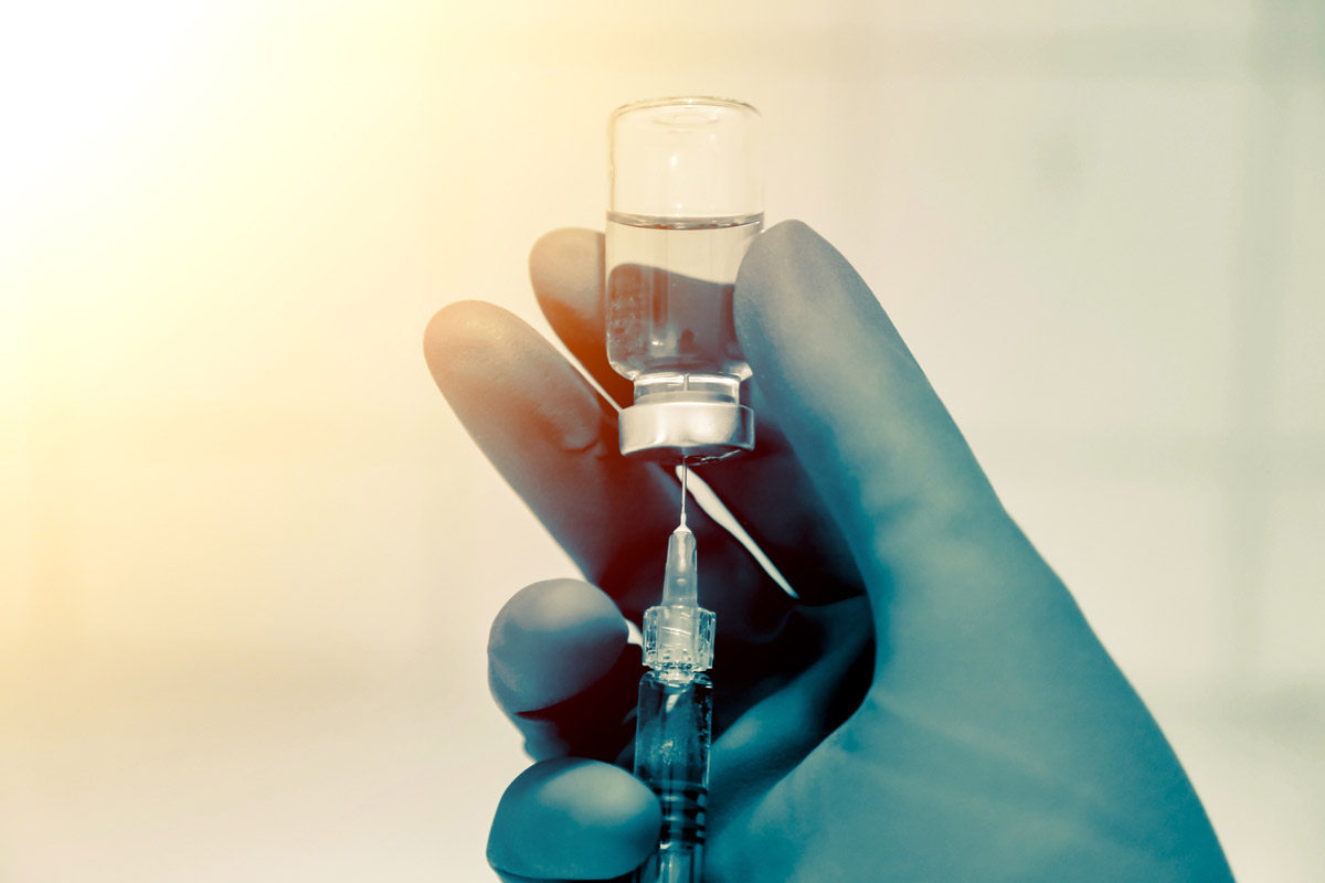 A gloved doctor's hand holding a syringe and vaccine vile.