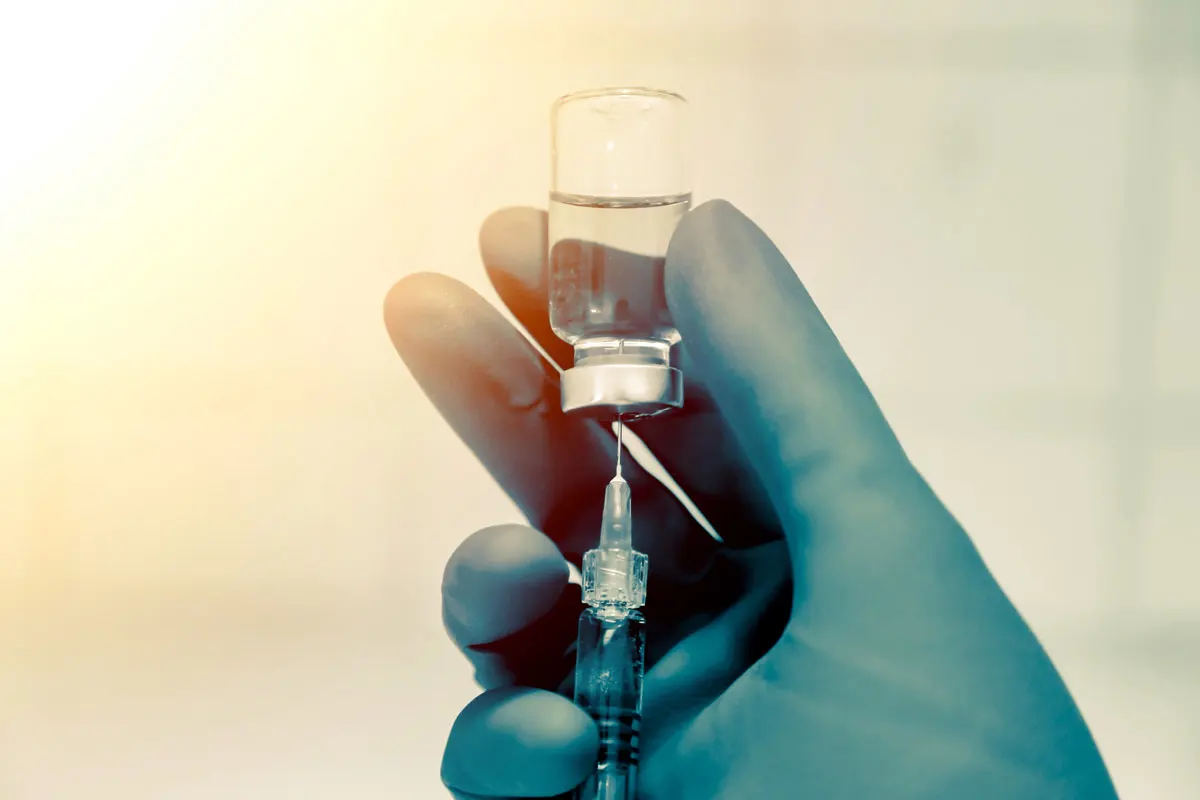 A gloved doctor's hand holding a syringe and vaccine vile.