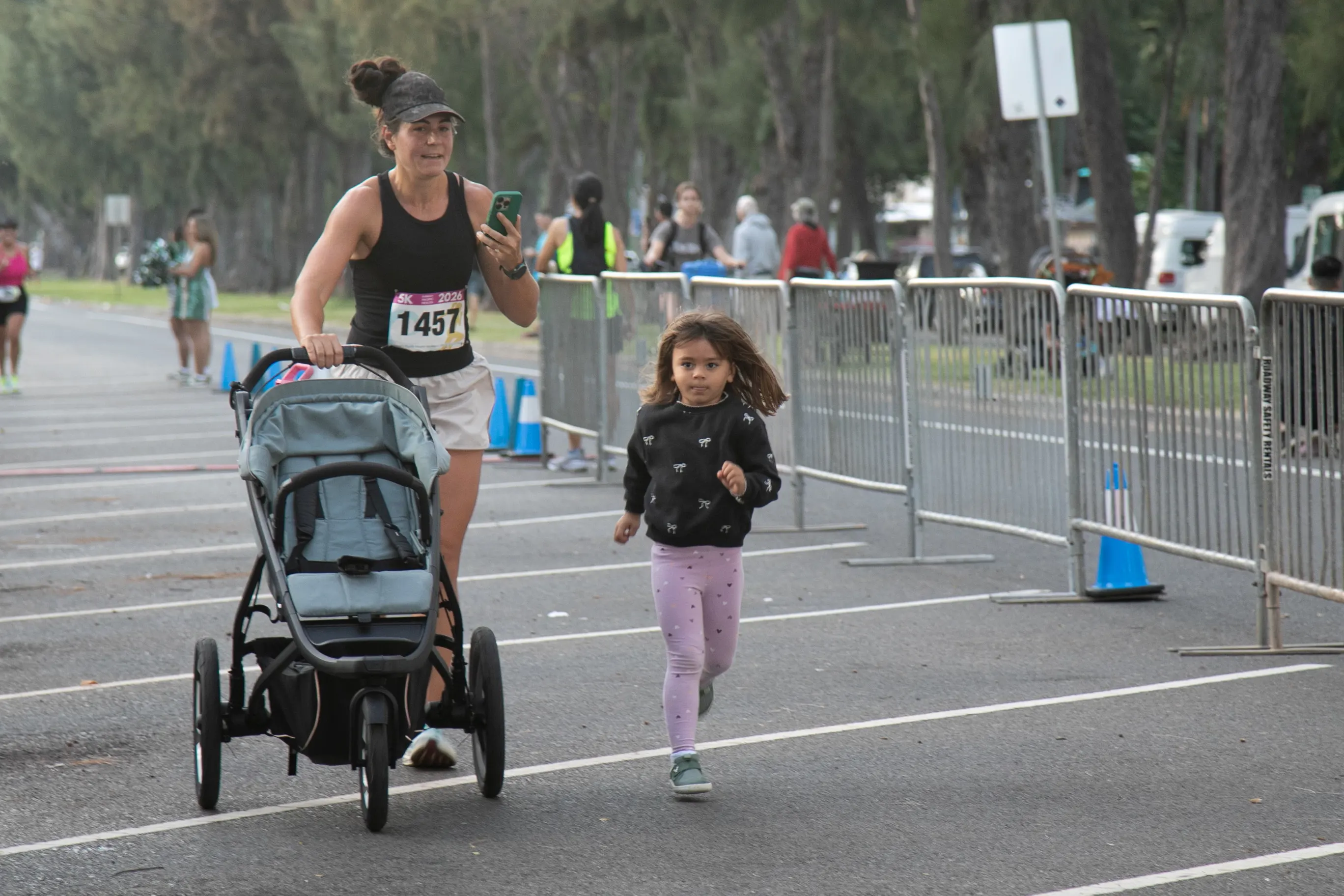 Young girl running alongside her mom as she pushes the stroller to the finish line.