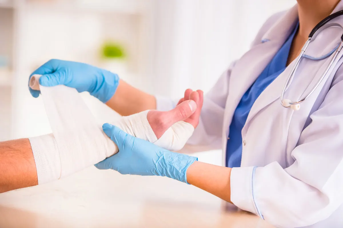 A female doctor wraps a male patient's hand in a bandage.
