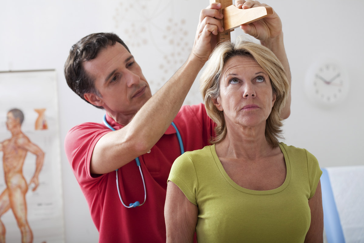An older woman having height measured by male nurse at the doctors' office.