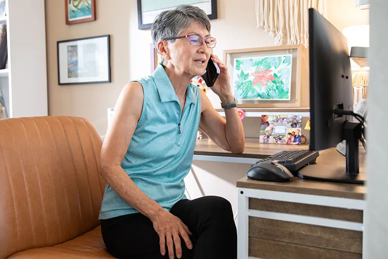 Woman talking on mobile phone while seated at computer.