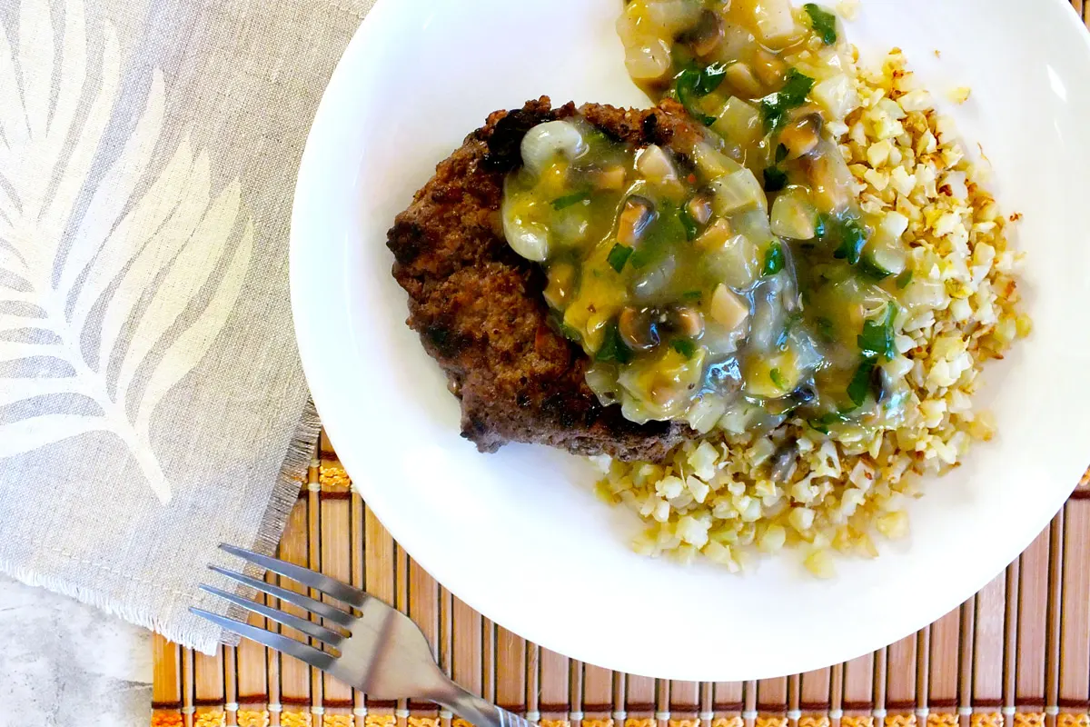 Lean ground sirloin, a vegetable gravy and cauliflower rice sit on a white plate.