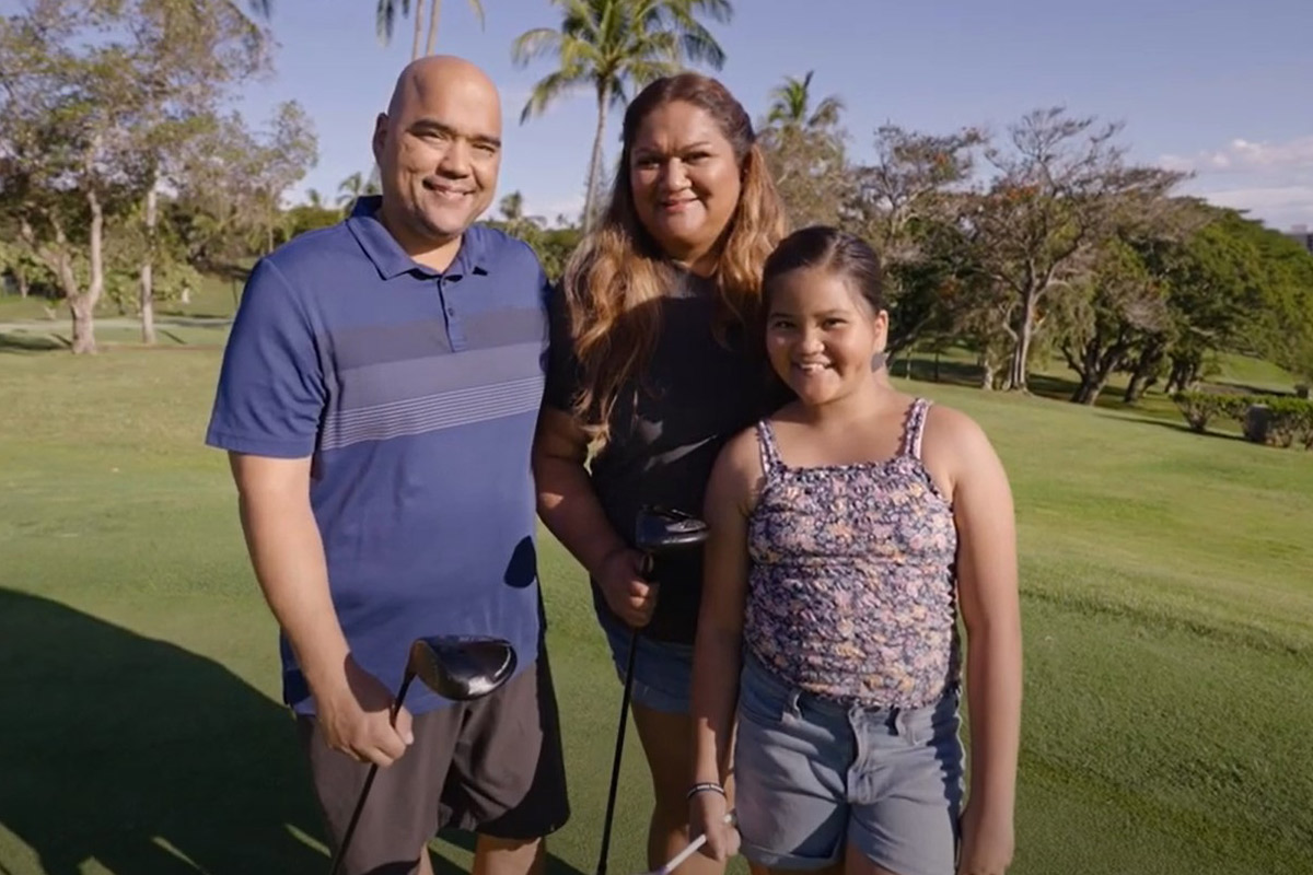 Father and mother smiling on a golf course with their daughter.