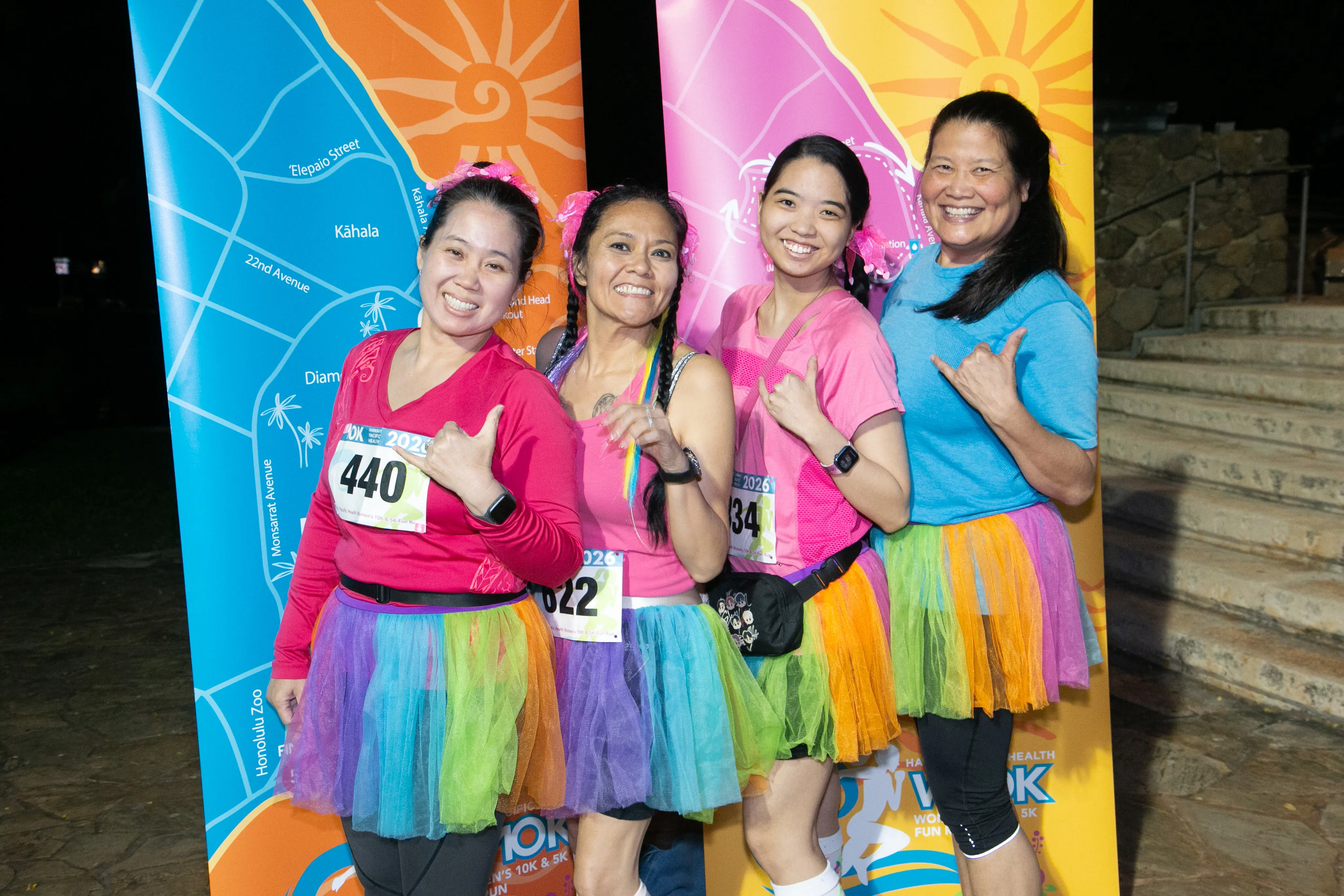 Group of race participants wearing matching rainbow-colored tutus posed in front of the course map.