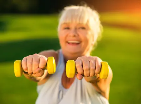 An older woman holds weights and smiles.