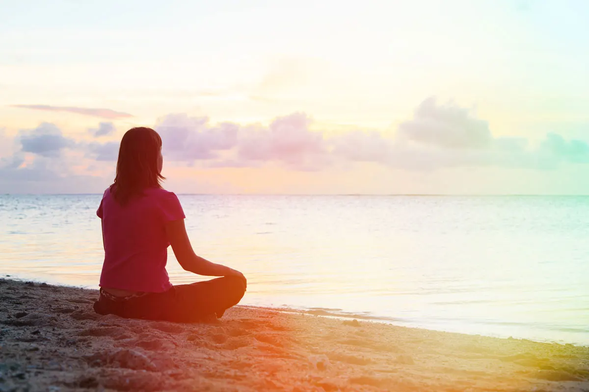 A lady on the beach sitting crossed legged during dawn.