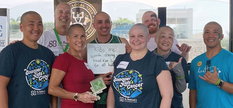 Group of shaved-head people in support of cancer research and kids battling cancer.