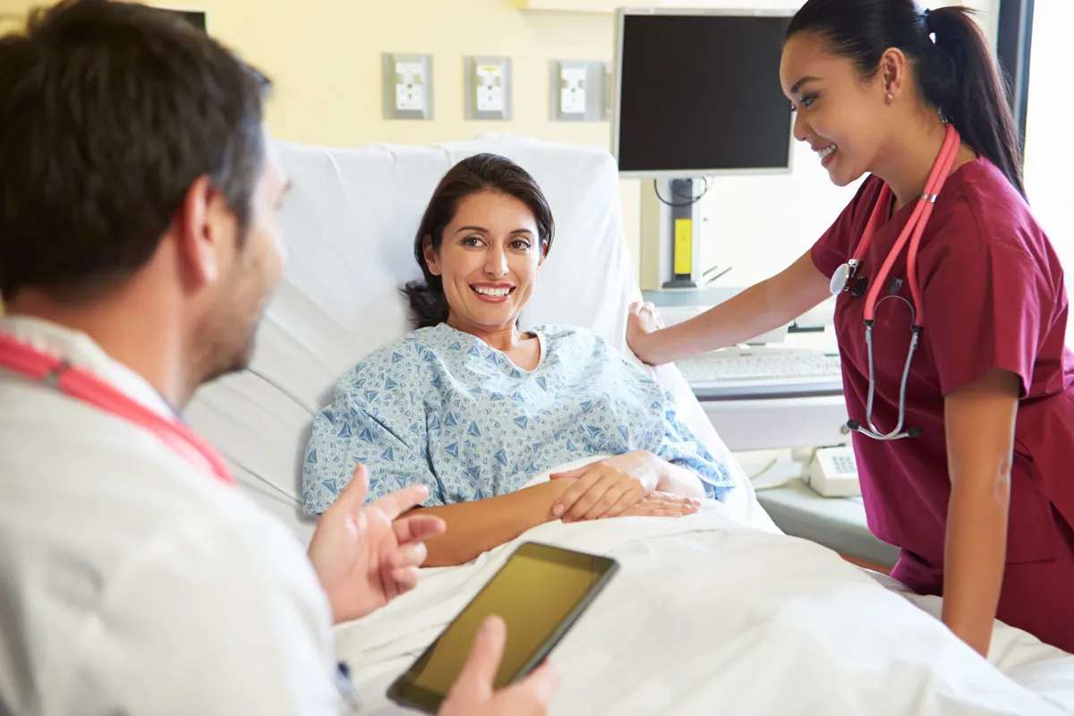 A doctor and nurse discussing treatment options with patient in hospital room.