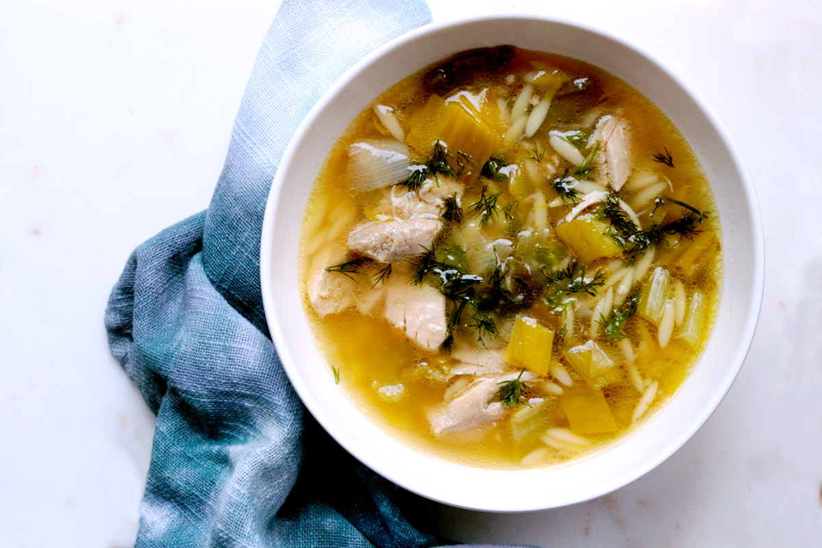 Golden broth, rich soup and green garnish sit in a white bowl with a blue napkin on a white table.