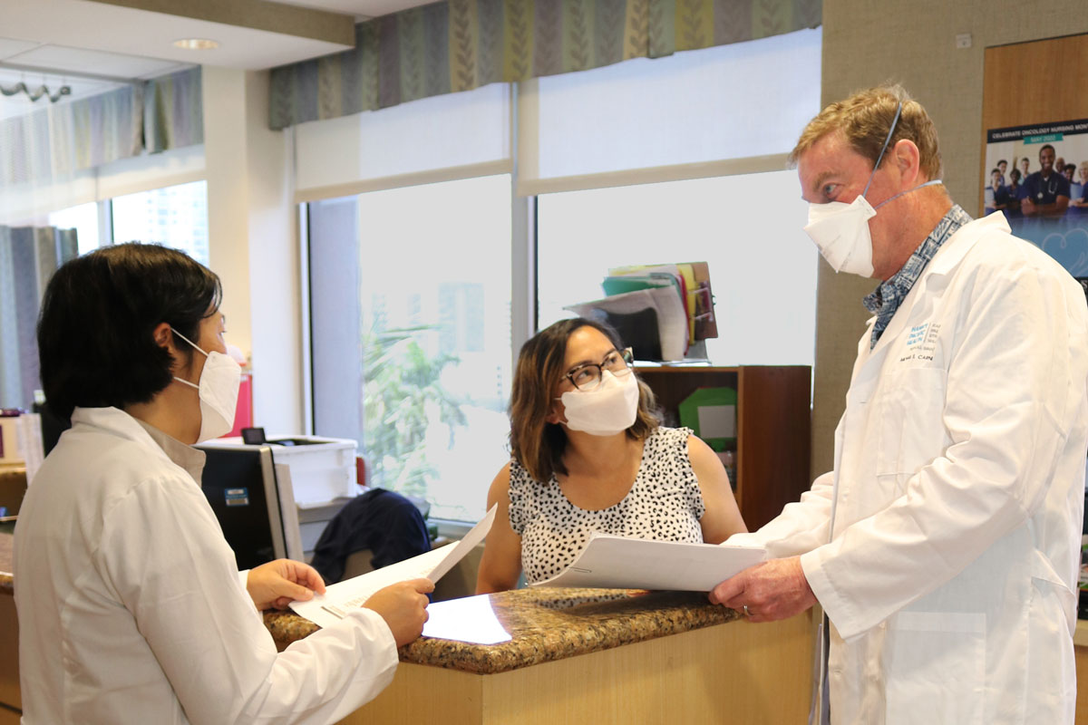 Physician speaking with two of his colleagues. All are wearing masks.