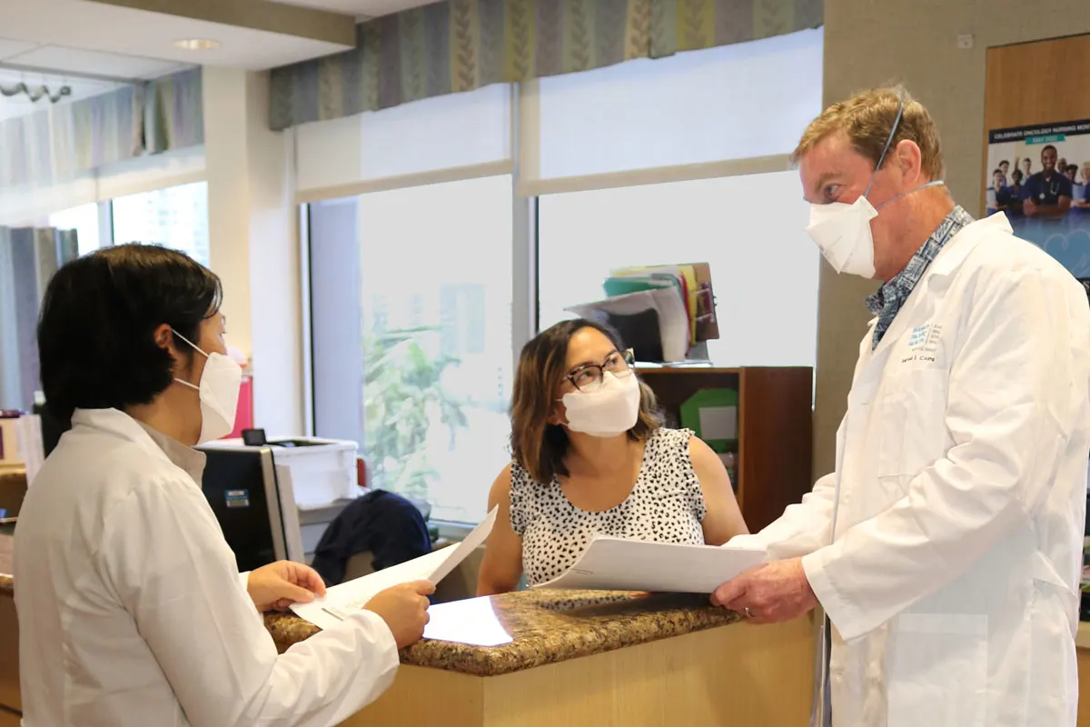 Physician speaking with two of his colleagues. All are wearing masks.
