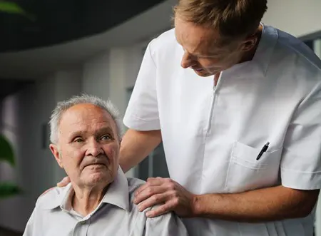 A care worker puts their hands on the shoulders of an older patient. 