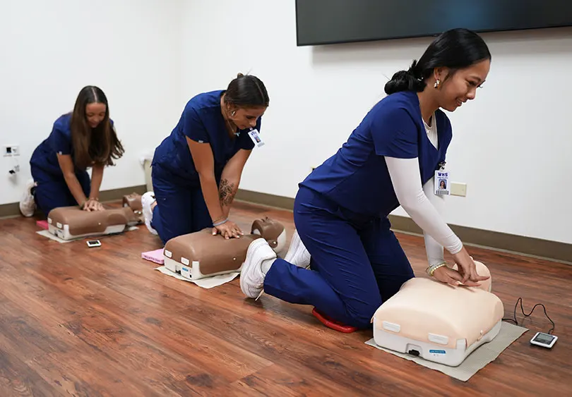 Three students practicing CPR on fake dummy patients.