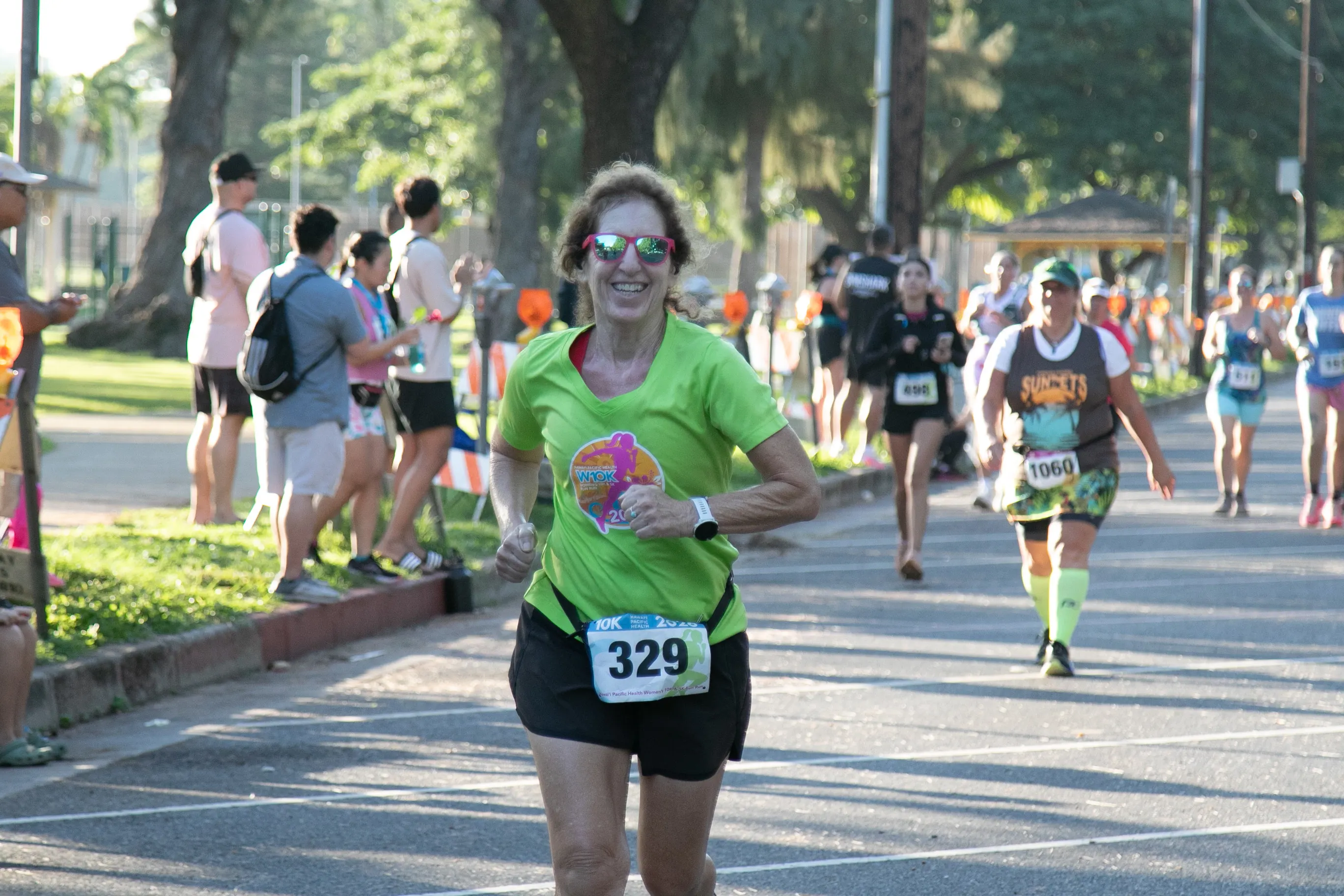 A 10K participant wearing the 2025 finisher shirt is smiling as she runs to the finish line.