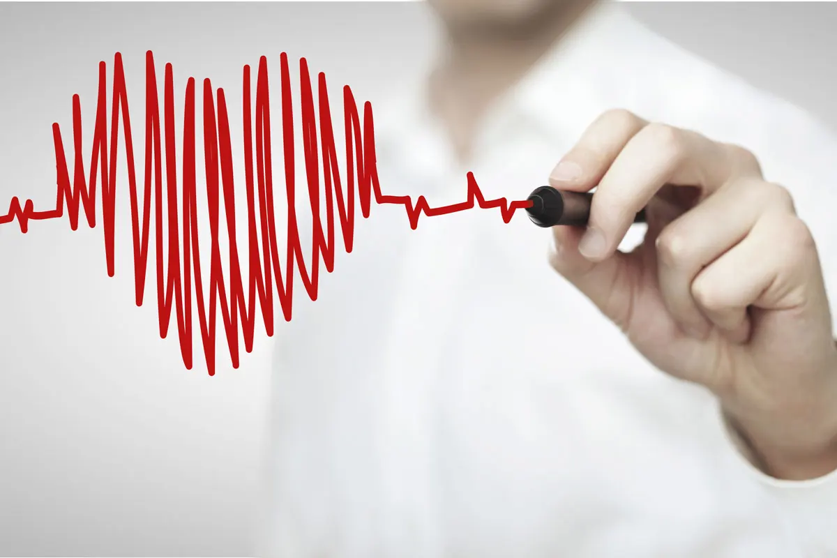 A doctor is making an illustration of a heart with EKG lines on a clear board.