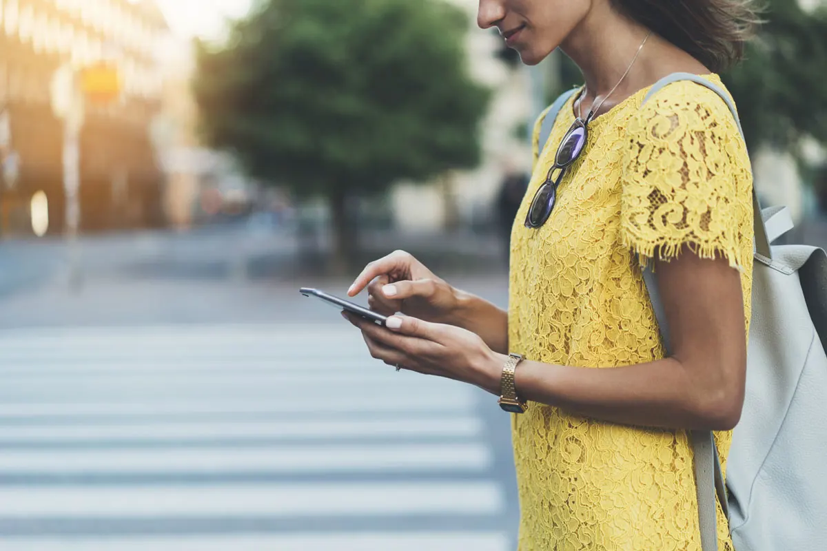 A young woman walking towards crossroads holding her mobile phone.