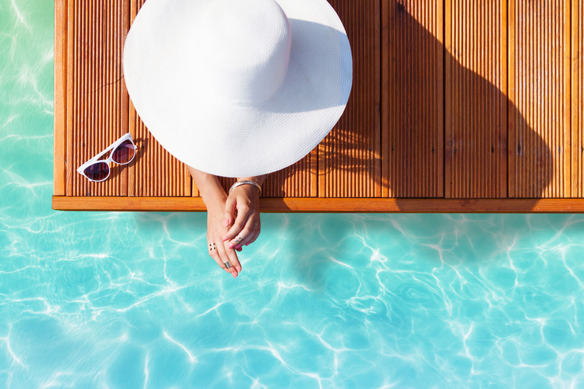 A woman with sunhat sitting by the pool.