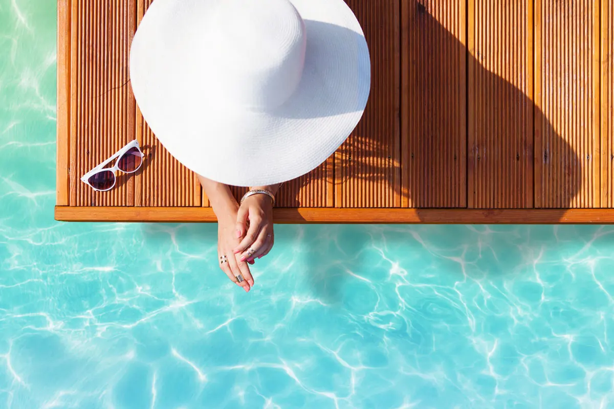 A woman with sunhat sitting by the pool.