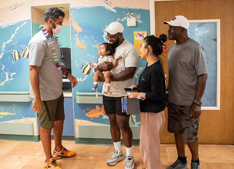 NFL Football player, Marcus Mariota talking to a family with a young child in the Kapiolani hallway.
