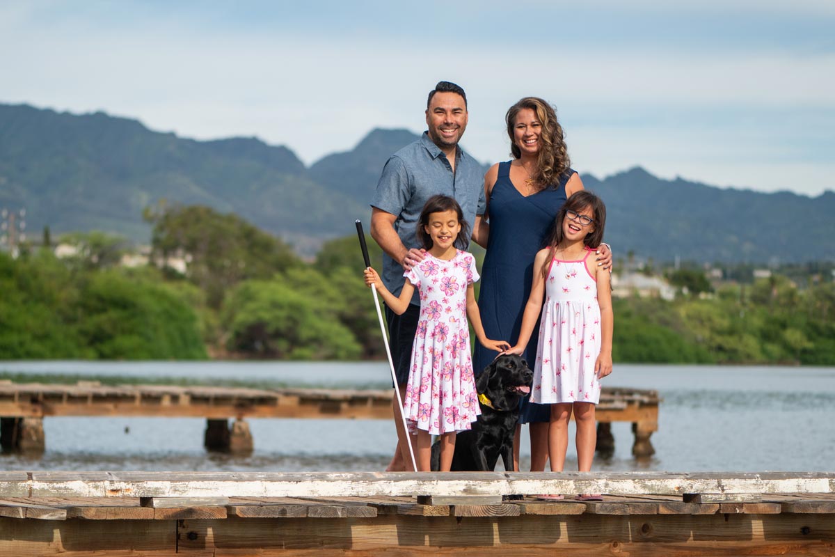 The Awa family happily standing on a dock with their dog.