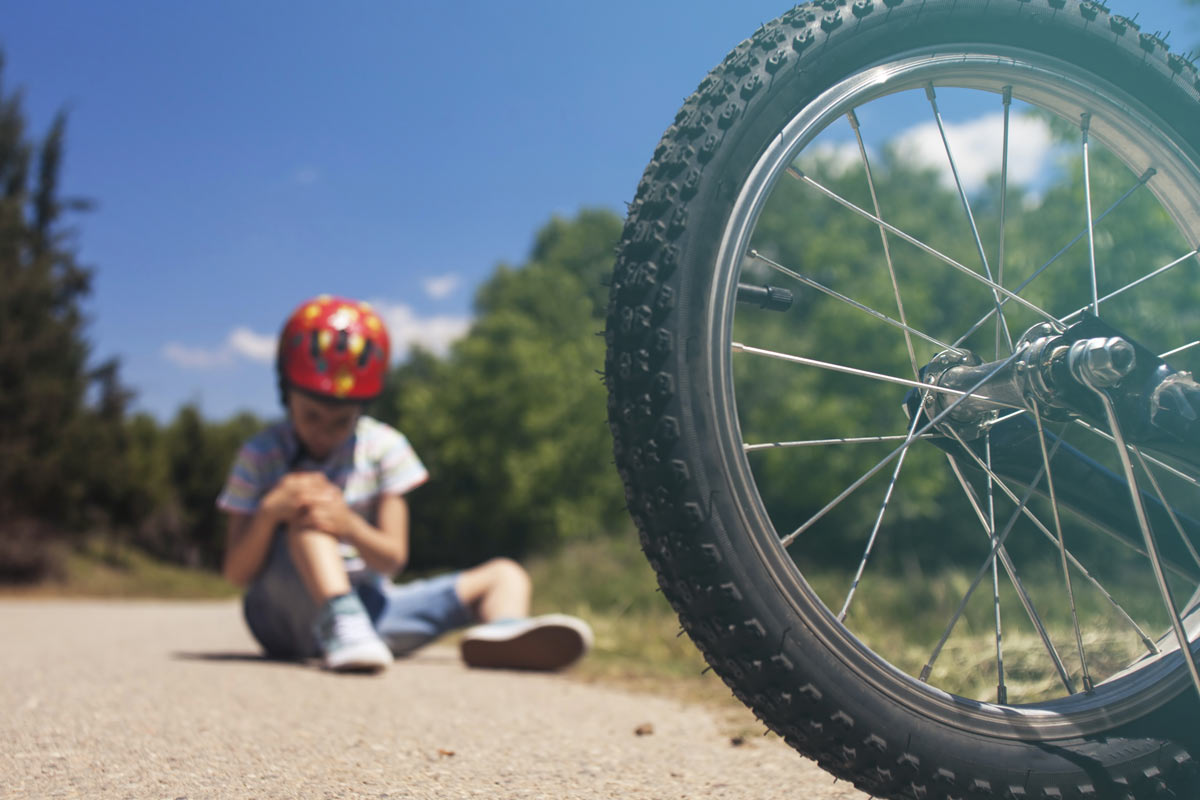 A child sits on the side of the road holding knee in pain after an e-bike accident.