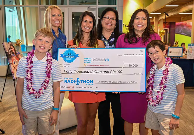 Small group of two young boys and four women smiling with a giant check for $40,000.