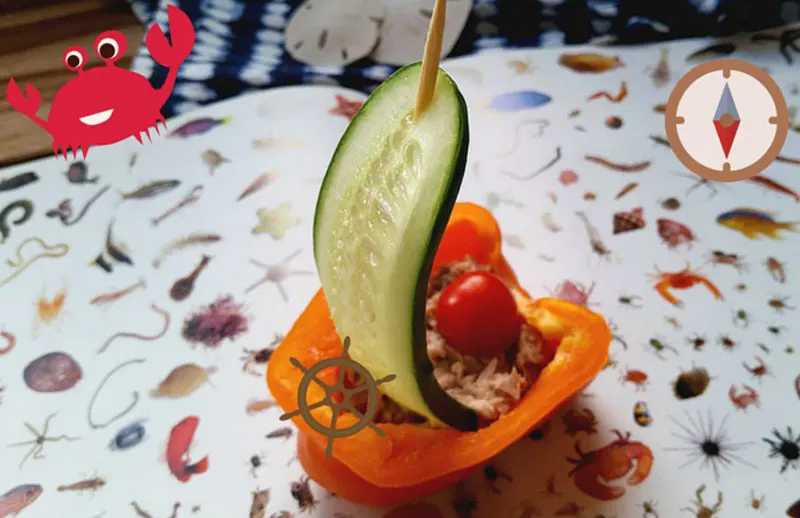 A sailboat made with a bell pepper hull, filled with tuna and tomato with a cucumber sail hung from a bamboo skewer.