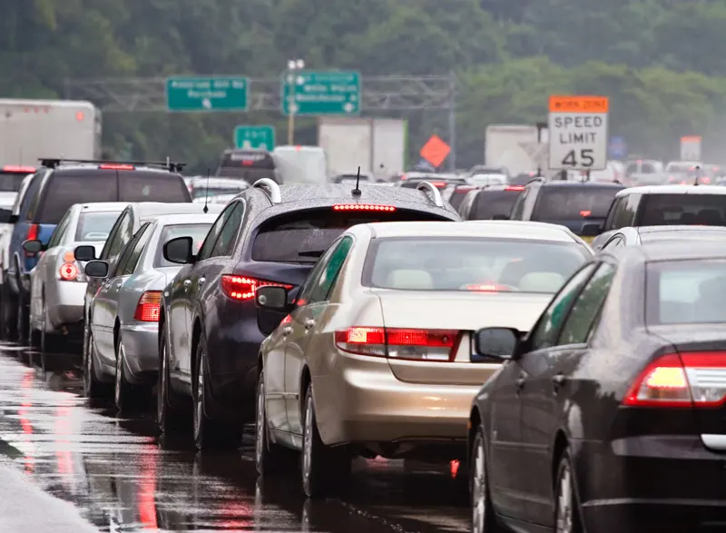 Cars sit on a wet highway in bumper to bumper traffic.