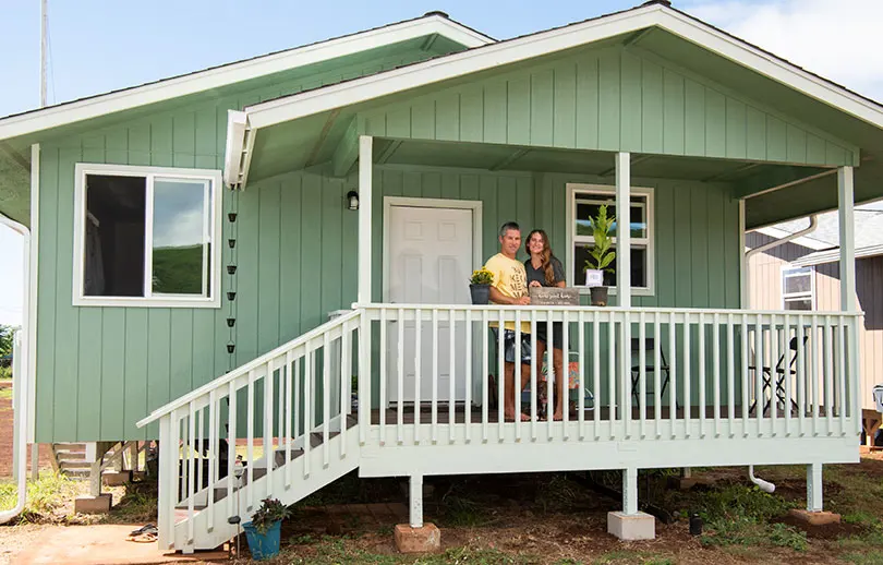Couple standing on the patio of their new sage green home.