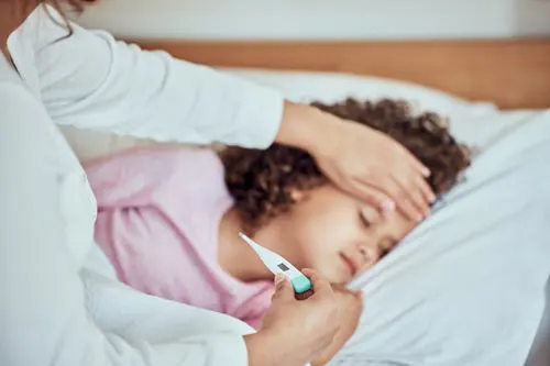 A parent touches a child's forehead while checking a thermometer.