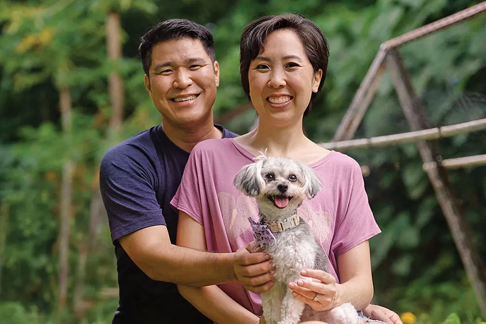 Woman in pink shirt holding and adorable doc with a pink collar alongside her husband.