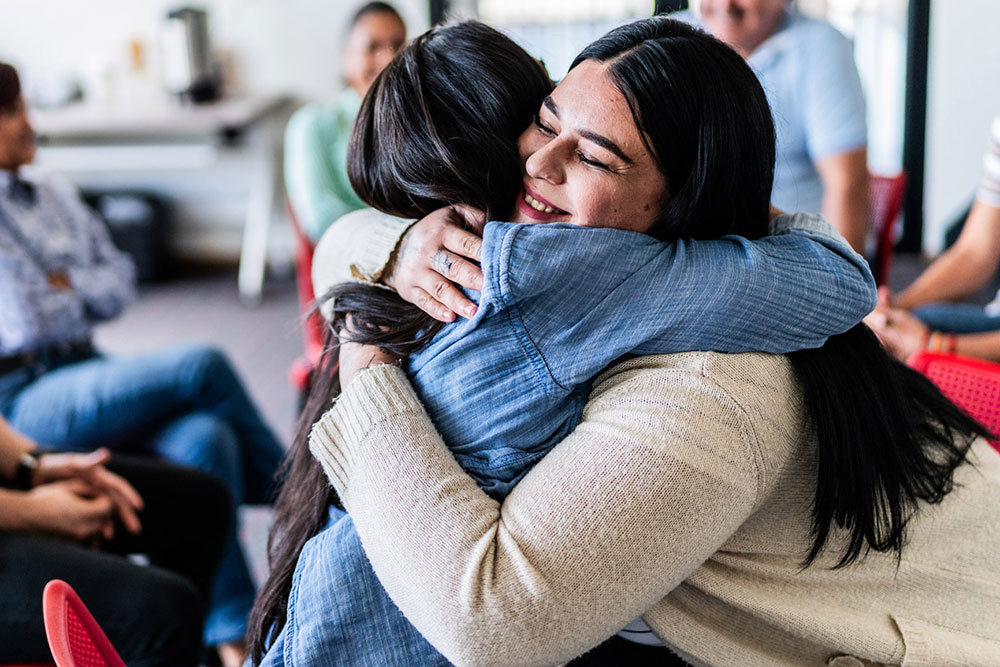 Two women hug each other during a support group meeting.