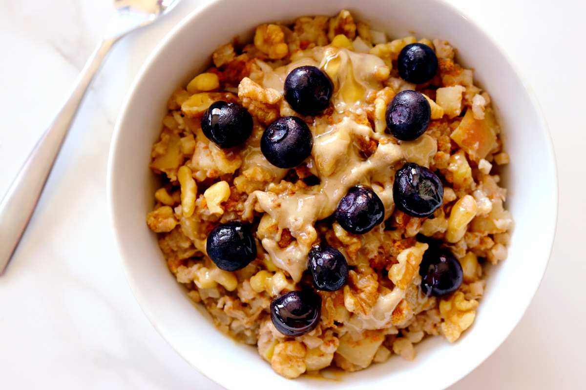 A bowl of Cauli-Oats topped with blueberries sits on a marble counter top with a spoon resting in the background.